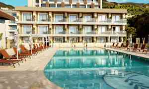 Bild av en pool med solstolar och parasoller framför ett modernt hotell med balkonger. (AI-genererad text)