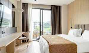 Ett hotellrum med en säng, skrivbord, stol och en balkongdörr med utsikt. (AI-genererad text)