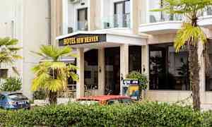 Byggnadens framsida med texten 'Hotel New Heaven', omgiven av palmer och en bankomat. (AI-genererad text)