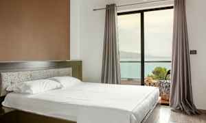 Ett hotellrum med en säng, ett fönster med gardiner och utsikt mot havet. (AI-genererad text)