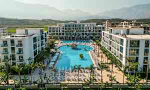 En modern hotellresort med en stor pool och omgivande solstolar, belägen i en grönskande dal med berg i bakgrunden. (AI-genererad text)