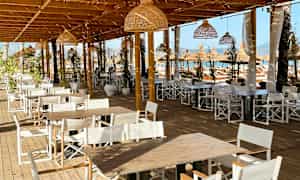 Bild på en utomhusservering med träbord och vita stolar under en träpergola. (AI-genererad text)