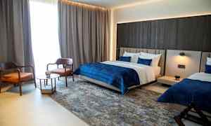 Ett modernt hotellrum med två sängar, en sittgrupp med två stolar och ett bord, samt mörka gardiner vid fönstret. (AI-genererad text)