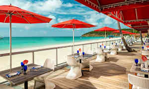 Utomhusservering med röda parasoller vid en sandstrand. (AI-genererad text)