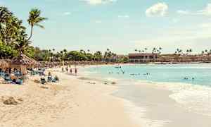 En sandstrand med palmer och solstolar, människor badar och promenerar, och havet sträcker sig ut under en klar himmel. (AI-genererad text)