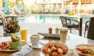 Frukost med grönsakswrap, fruktsallad och drycker vid ett poolområde utomhus. (AI-genererad text)