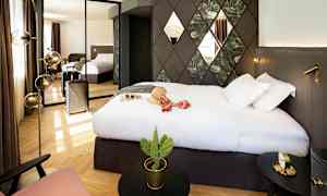 Ett hotellrum med en stor säng, väggdekorationer och en spegel som reflekterar rummet. En resväska står vid sidan och det finns en liten kaktus på ett bord. (AI-genererad text)