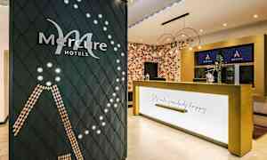Receptionen på ett Mercure-hotell med företagets logotyp synlig på en dekorativ vägg och en reception med texten "Let's make somebody happy". (AI-genererad text)