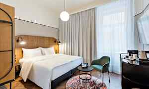 Ett hotellrum med en dubbelsäng, en stol och ett bord samt en stor fönster med gardiner. (AI-genererad text)