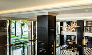 En elegant hotellobby med moderna detaljer, mörka pelare, och stora fönster med utsikt mot gatan utanför. (AI-genererad text)