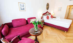 Ett hotellrum med en röd soffa, ett runt bord med en blomsterbukett och en säng med röda detaljer. (AI-genererad text)