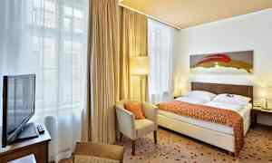 Ett hotellrum med en dubbelsäng, en fåtölj, ett bord med en TV på och stora fönster med gardiner. (AI-genererad text)