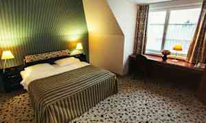 Ett hotellrum med en dubbelsäng, randigt överkast, två sängbord med lampor och en arbetsbänk med stol vid ett fönster. (AI-genererad text)