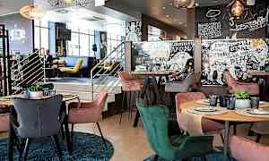 En modern interiör av en restaurang med färgglada stolar runt bord som har dukade tallrikar och glas. Väggarna är dekorerade med konstnärliga mönster och texter. (AI-genererad text)