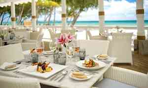 En dukad restaurangbord nära stranden med tallrikar, glas och blommor. (AI-genererad text)