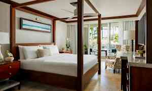 En elegant sovrum med en himmelssäng, sittmöbler och utsikt över grönska genom öppna glasdörrar. (AI-genererad text)