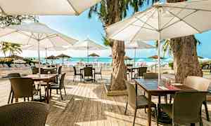 Uteservering med trämöbler och parasoller belägen nära stranden med utsikt över havet. (AI-genererad text)