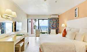 Hotellrum med en stor säng, skrivbord, stolar och en balkong med utsikt över havet. (AI-genererad text)