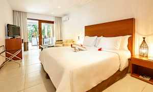 Ett hotellrum med stor säng, TV, sittplats och en terrass med utsikt mot en trädgård. (AI-genererad text)