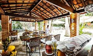 En öppen restaurang med trä- och tegelstruktur, där mat och brickor är upplagda på ett bord tillsammans med fruktdrycker. En person står vid ett bord. (AI-genererad text)