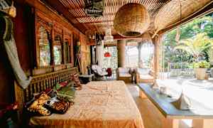 Uteplats med exotisk inredning, inklusive dekorativa trämöbler, korgstolar och gröna växter. (AI-genererad text)