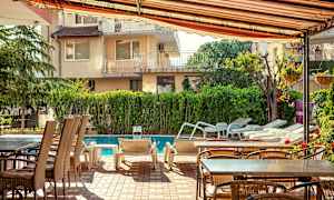 Utemöbler och solstolar vid en pool, omgiven av grönska och byggnader. (AI-genererad text)