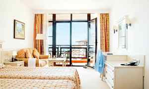 Ett hotellrum med två enkelsängar, en soffa, ett skrivbord och en balkong med utsikt. (AI-genererad text)