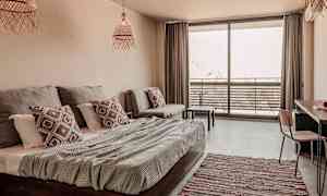 Ett ljust och modernt hotellrum med säng, soffa och en balkong med utemöbler. (AI-genererad text)