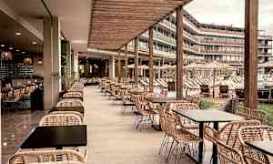 En utomhusrestaurang med rottingmöbler och utsikt över en pool och solstolar. (AI-genererad text)