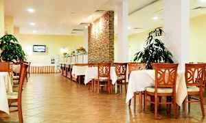 Bild på en matsal med bord och stolar av trä, vitbordduk, växter och en buffésektion. (AI-genererad text)