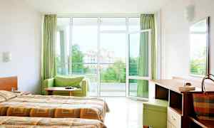 Hotellrum med dubbelsängar, skrivbord samt öppet fönster mot en balkong med utsikt. (AI-genererad text)