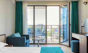 Modernt hotellrum med en säng, sittgrupp och glasdörrar mot en balkong. (AI-genererad text)