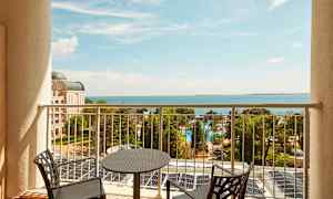 Utsikt från en balkong mot havet, med stolar och bord i förgrunden. (AI-genererad text)