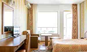 Ett hotellrum med två sängar, ett träskrivbord med en TV på, ett litet soffhörn med soffbord och en balkong i bakgrunden. (AI-genererad text)