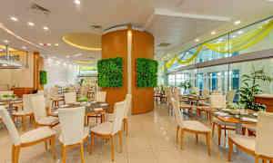 En restaurangs interiör med flera bord och stolar, dekorativa väggpaneler med grönska och stora glasväggar. (AI-genererad text)