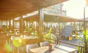 En utomhusrestaurang med bord, stolar och en lekplats för barn under ett tak. (AI-genererad text)