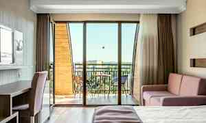 Ett ljus hotellrum med balkong, möblerat med bädd, soffa och skrivbord. (AI-genererad text)