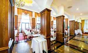 En elegant restaurang med dukade bord, mörka trägolv och stora fönster med gardiner. (AI-genererad text)