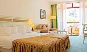 Ett hotellrum med en dubbelsäng, sittgrupp med fåtölj och bord, samt en balkong med möbler och utsikt. (AI-genererad text)