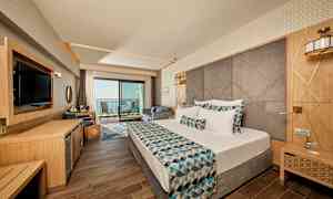 Hotellrum med modern inredning, dubbelsäng och balkong med havsutsikt. (AI-genererad text)