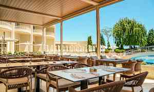 Utomhusrestaurang med bord och stolar under tak, omgiven av grönt och en pool i bakgrunden. (AI-genererad text)