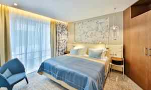 Ett hotellrum med en dubbelsäng, blått sängöverkast och dekorativ vägg bakom sängen. (AI-genererad text)