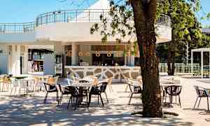 En utomhusbar med bord och stolar under träd, med ljus inredning och trädetaljer. (AI-genererad text)