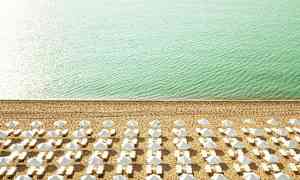 Strand med solstolar och parasoller ordnade i rader nära turkost hav. (AI-genererad text)