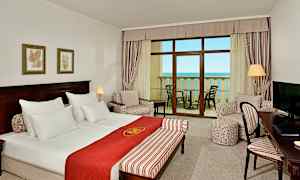 Ett hotellrum med dubbelsäng, sittgrupp, ett skrivbord och balkong med havsutsikt. (AI-genererad text)