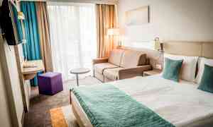 En modern hotellrum med en dubbelsäng, soffa, och fönster med gardiner. (AI-genererad text)