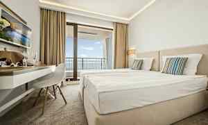 Hotellrum med två sängar, skrivbord och balkong med utsikt över havet. (AI-genererad text)