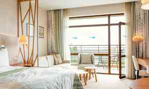 Ett hotellrum med säng, sittgrupp, bord och öppen balkongdörr. (AI-genererad text)