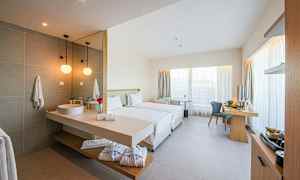 Ett modernt hotellrum med två enkelsängar, skrivbord och integrerat badrum med handfat. (AI-genererad text)