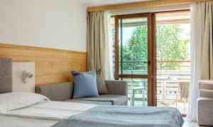 Ett hotellrum med en säng, soffa och balkongmöbler synliga genom en glasdörr. (AI-genererad text)